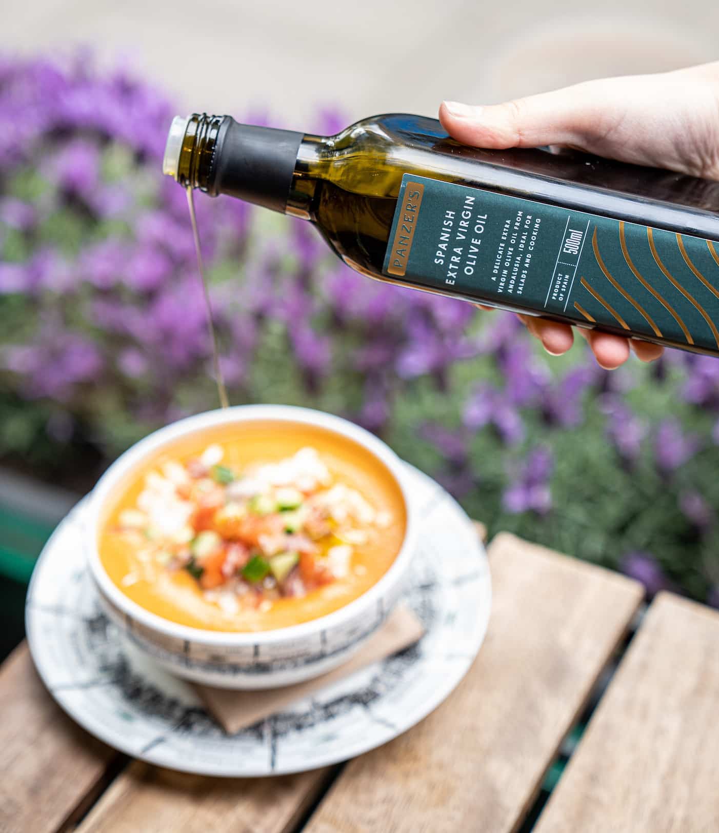 Panzer's Olive Oil being poured on a bowl of orange gazpacho soup