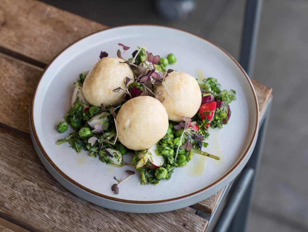 A plate of ricotta gnudi with bright garden peas and radishes on a wooden table