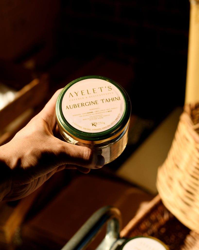 A jar of ayelet's kosher aubergine tahini held by a hand in sunlight