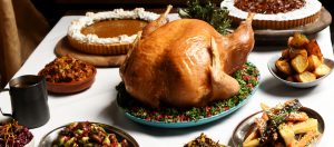 Spread of thanksgiving staples, roast turkey, pumpkin & pecan pies, roasted carrots & parsnips, stuffing, sprouts on a white tablecloth