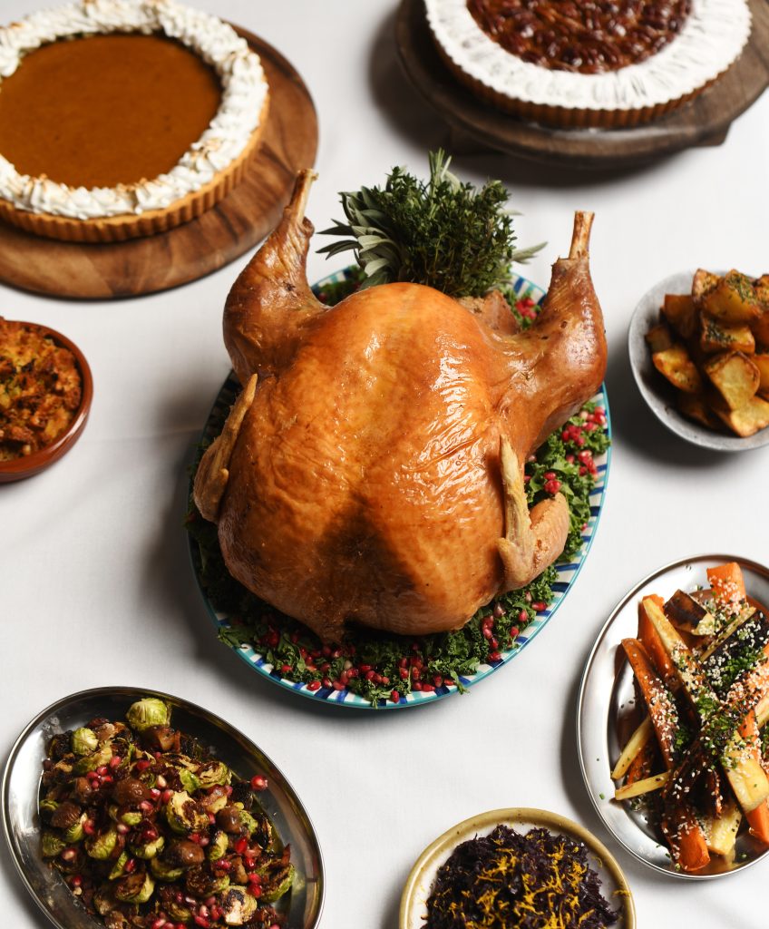 Spread of thanksgiving staples, roast turkey, pumpkin & pecan pies, roasted carrots & parsnips, stuffing, sprouts on a white tablecloth