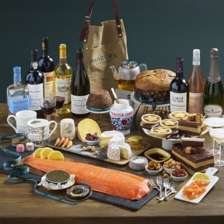 A festive display from Panzer’s Grand Epicurean Christmas hamper, featuring fine wines and spirits, artisan cheeses, panettone, Christmas pudding, and gourmet condiments. The arrangement includes Panzer’s signature mugs and apron, capturing the elegance and indulgence of a true luxury hamper from Panzer’s London.